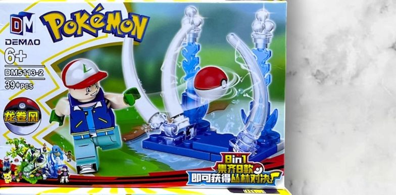 Figura armable de entrenador Pokémon con gorra roja y pokebola sobre plataforma de batalla, set DEMAO DM5113-2 de 39 piezas